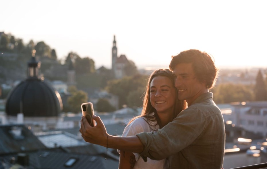 Paar macht ein Selfie mit der atemberaubenden Aussicht auf die historische Stadt Salzburg im Hintergrund